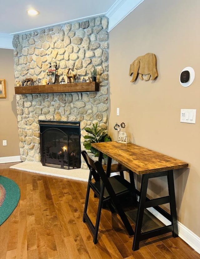 dining space featuring ornamental molding, a stone fireplace, baseboards, and wood finished floors