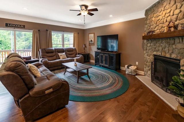 living area featuring a fireplace, a ceiling fan, baseboards, dark wood finished floors, and crown molding