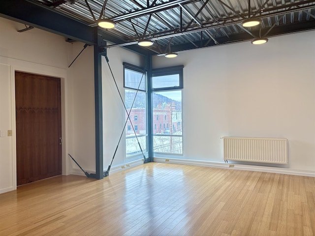 spare room featuring radiator heating unit, baseboards, and wood finished floors