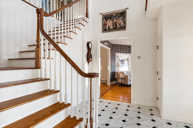 stairway with a baseboard radiator, a towering ceiling, baseboards, and tile patterned floors