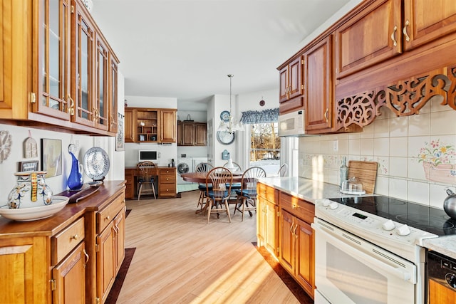 kitchen featuring white appliances, glass insert cabinets, light wood-style floors, pendant lighting, and backsplash