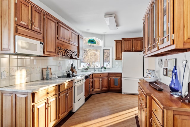 kitchen featuring white appliances, light wood-style flooring, glass insert cabinets, brown cabinets, and a sink