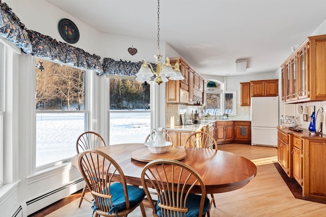 dining area featuring light wood-type flooring, a baseboard radiator, a chandelier, and a wealth of natural light