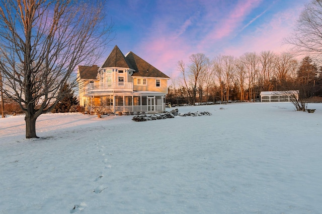 snow covered back of property featuring a sunroom