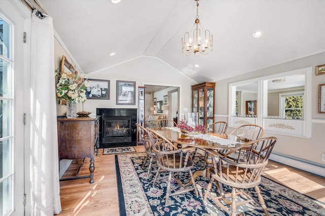 dining room featuring light wood finished floors, a fireplace with flush hearth, ornamental molding, vaulted ceiling, and a chandelier