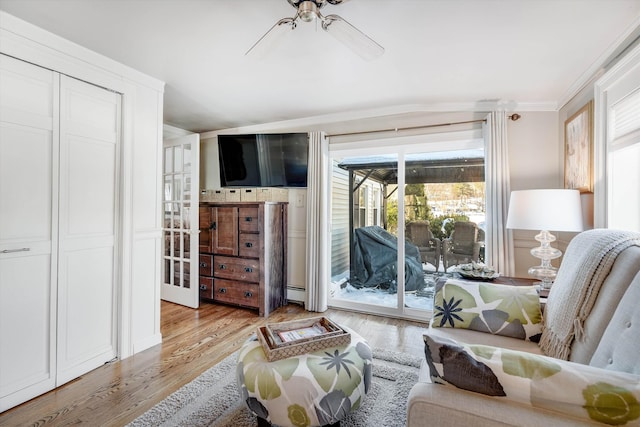 living area with light wood-type flooring, a baseboard heating unit, ceiling fan, and ornamental molding