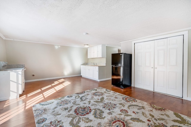 interior space featuring a textured ceiling, dark wood-type flooring, freestanding refrigerator, and baseboards