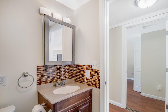 half bathroom featuring baseboards, wood finished floors, vanity, and decorative backsplash