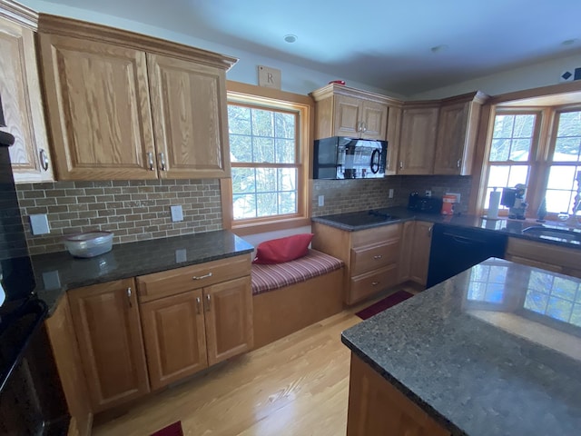 kitchen featuring a sink, light wood-type flooring, backsplash, black appliances, and dark stone countertops