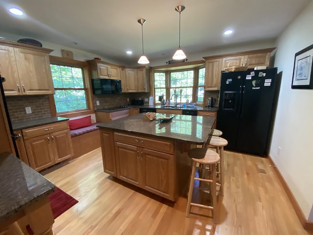 kitchen featuring a center island, a kitchen bar, light wood-style flooring, decorative backsplash, and black appliances