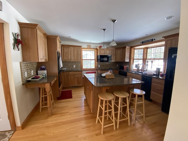 kitchen with a kitchen breakfast bar, hanging light fixtures, a center island, black appliances, and brown cabinetry