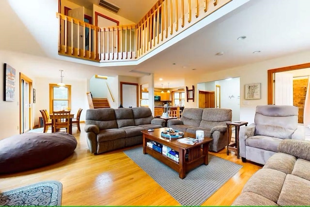 living area featuring a towering ceiling, light wood-style flooring, stairs, and visible vents