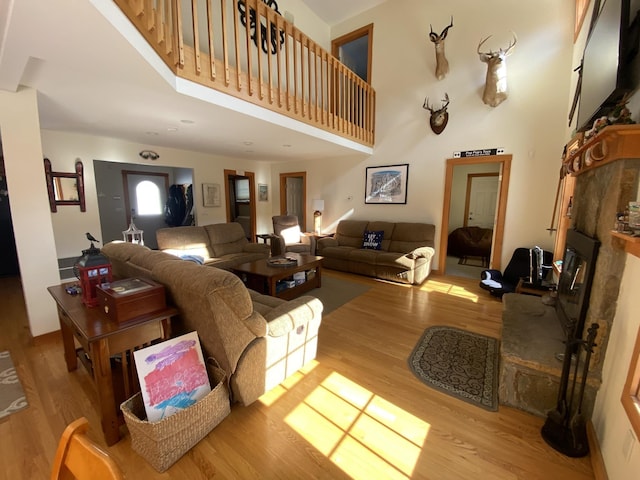 living area featuring a towering ceiling, a glass covered fireplace, and light wood-style flooring