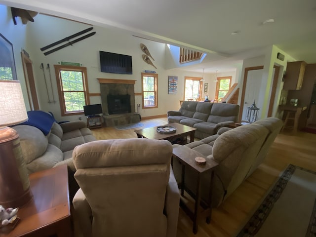 living room featuring lofted ceiling, light wood-style flooring, stairs, and a glass covered fireplace