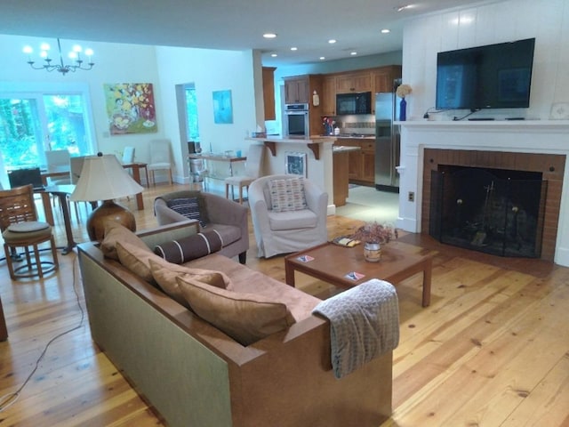 living room featuring a notable chandelier, a large fireplace, light wood-type flooring, and recessed lighting