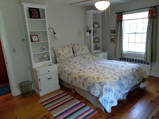 bedroom with radiator heating unit, dark wood finished floors, a ceiling fan, and baseboards