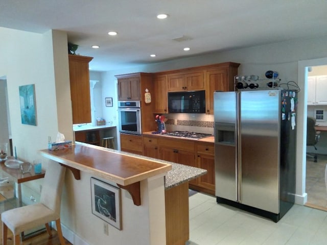 kitchen featuring a peninsula, a breakfast bar, brown cabinets, and stainless steel appliances