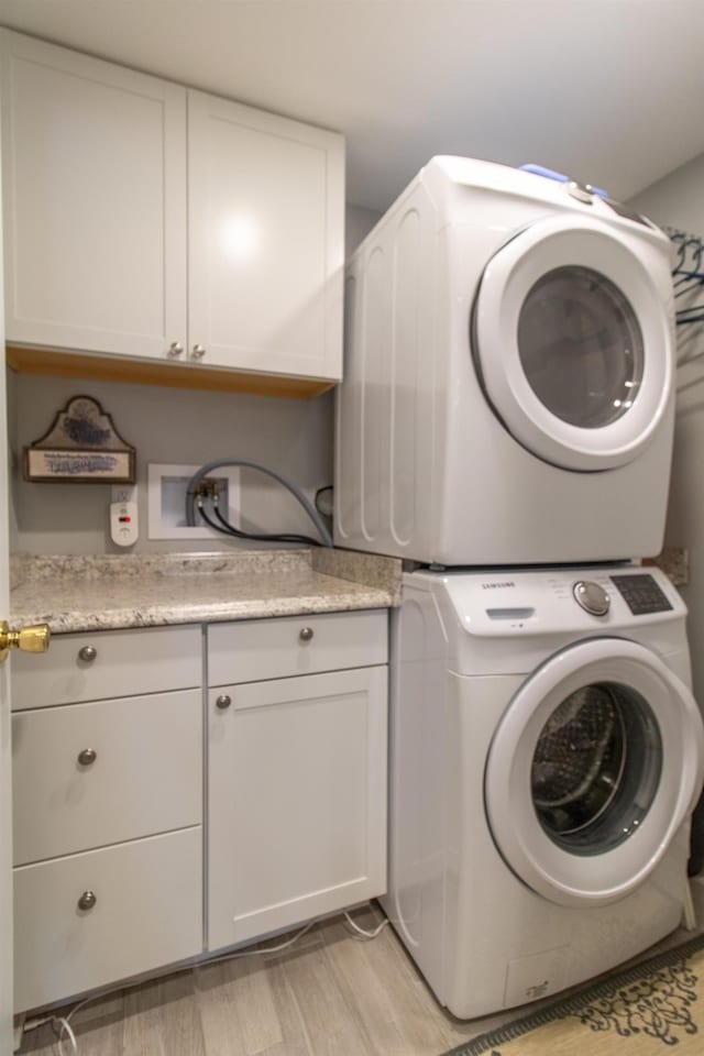 laundry room featuring cabinet space, light wood finished floors, and stacked washing maching and dryer