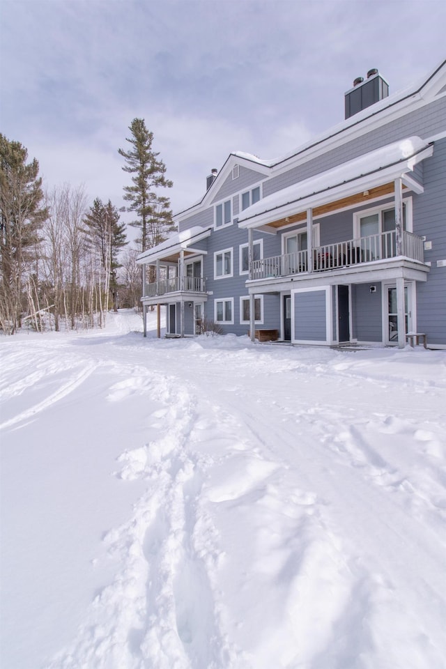 snow covered back of property with a garage, a chimney, and a balcony