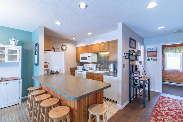 kitchen with white appliances, a sink, backsplash, brown cabinetry, and a kitchen bar