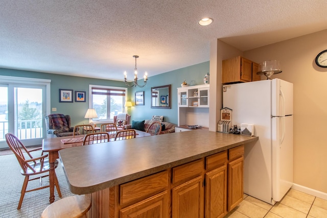 kitchen featuring dark countertops, brown cabinets, open floor plan, freestanding refrigerator, and hanging light fixtures