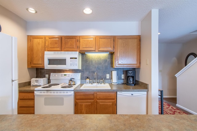 kitchen with brown cabinets, backsplash, a sink, a textured ceiling, and white appliances