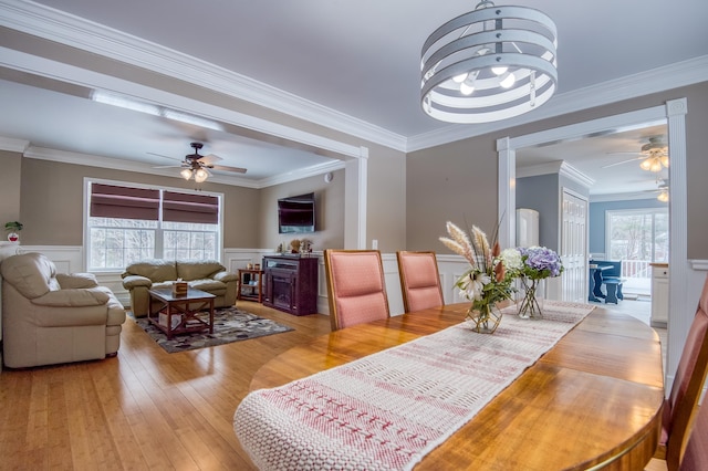 dining room with a ceiling fan, wainscoting, crown molding, and light wood-style flooring