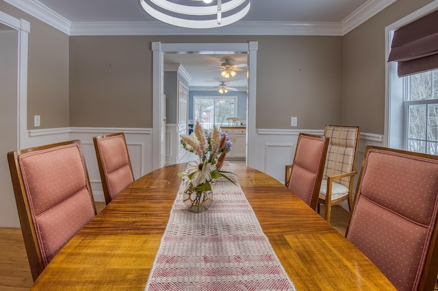 dining space with a wainscoted wall, a ceiling fan, ornamental molding, and wood finished floors