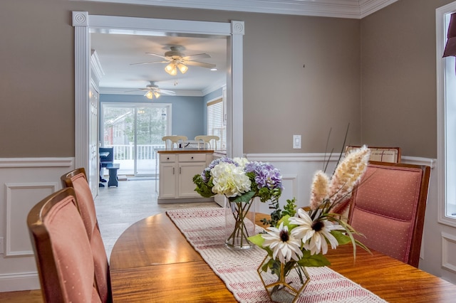 dining space featuring light wood-type flooring, ornamental molding, a decorative wall, and wainscoting