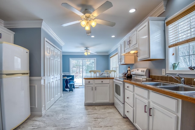 kitchen with white appliances, white cabinets, dark countertops, a peninsula, and a sink