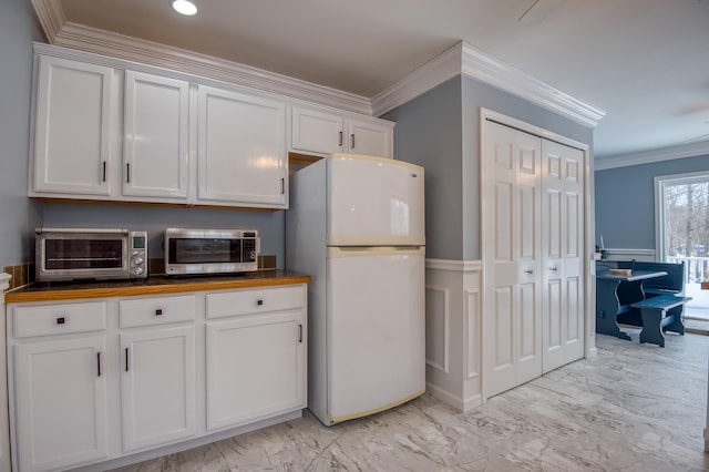 kitchen with a toaster, butcher block countertops, white cabinetry, freestanding refrigerator, and crown molding