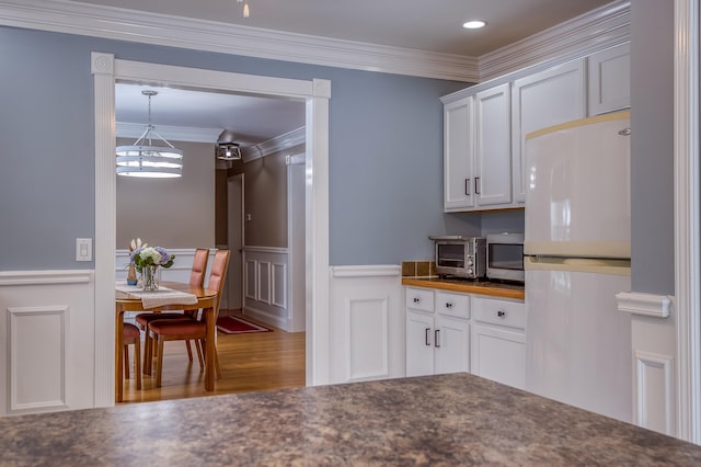 kitchen featuring ornamental molding, stainless steel microwave, freestanding refrigerator, and white cabinets