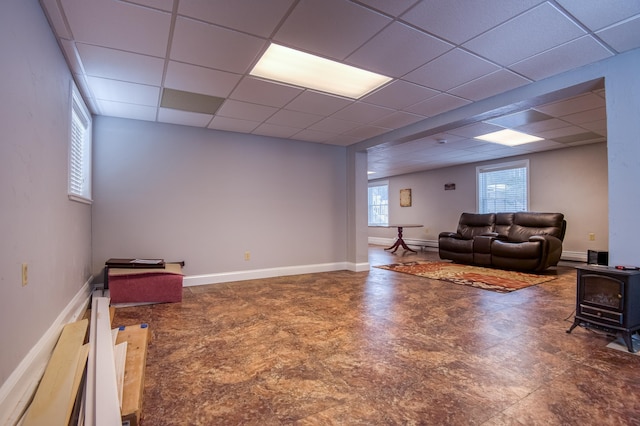 living room with a wood stove, a drop ceiling, and baseboards