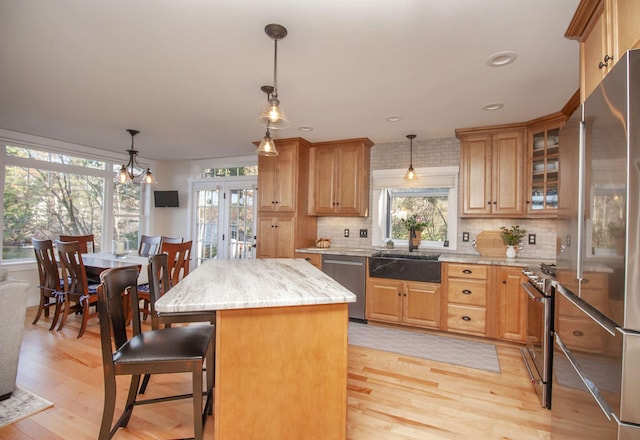 kitchen featuring hanging light fixtures, a kitchen island, appliances with stainless steel finishes, and glass insert cabinets