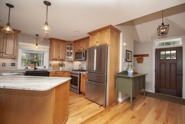 kitchen with appliances with stainless steel finishes, pendant lighting, glass insert cabinets, and a sink