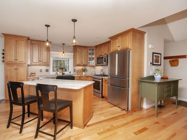 kitchen with light wood finished floors, glass insert cabinets, stainless steel appliances, and a sink