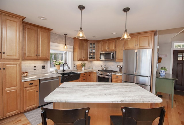 kitchen featuring decorative light fixtures, light wood-style flooring, appliances with stainless steel finishes, glass insert cabinets, and a sink