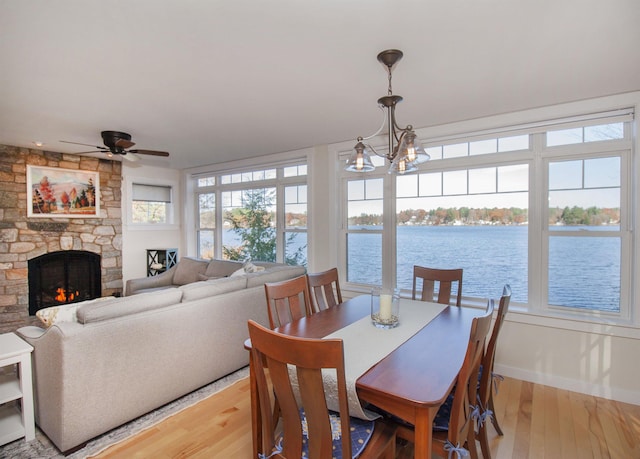 dining room with ceiling fan with notable chandelier, light wood-type flooring, a water view, and a fireplace