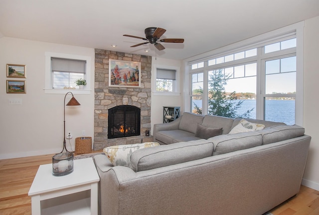 living area with a water view, a healthy amount of sunlight, wood finished floors, and a stone fireplace