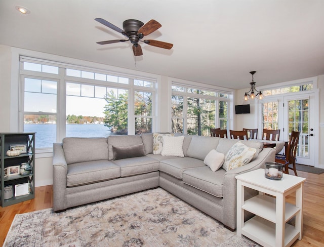 living area with a water view, light wood-style floors, and ceiling fan with notable chandelier