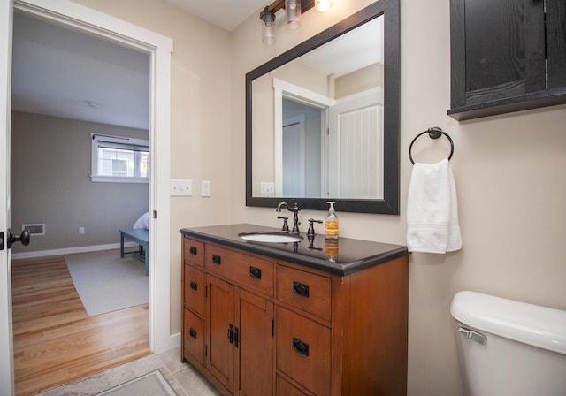 bathroom featuring visible vents, baseboards, toilet, wood finished floors, and vanity