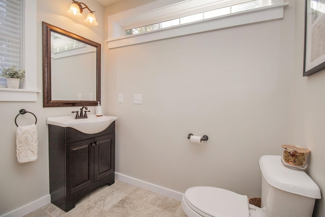 half bath featuring baseboards, vanity, and toilet