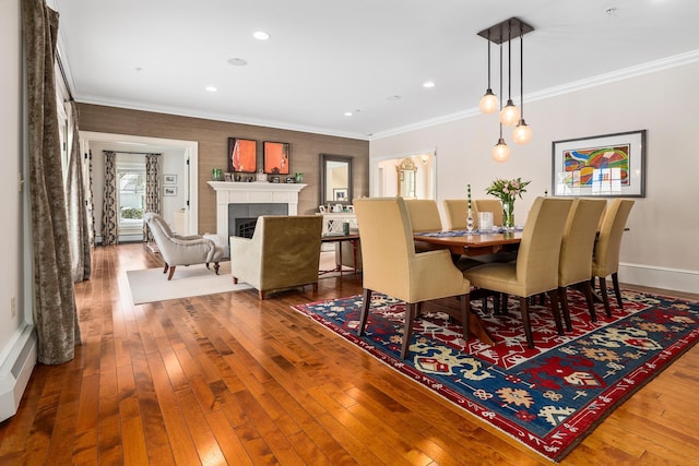 dining area with baseboards, ornamental molding, wood finished floors, and a tile fireplace