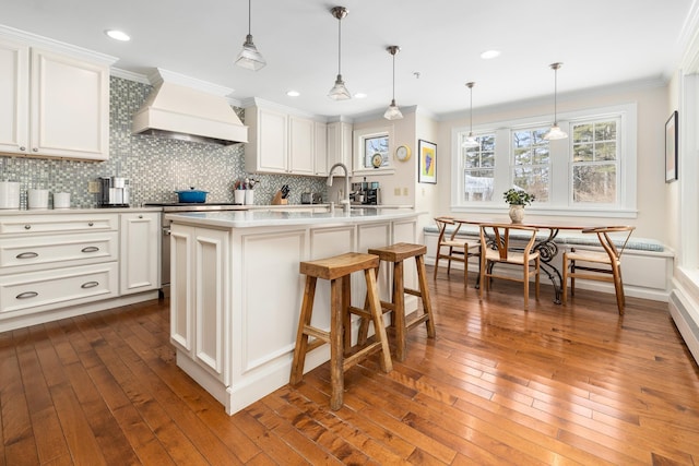 kitchen featuring pendant lighting, a center island with sink, breakfast area, white cabinetry, and premium range hood