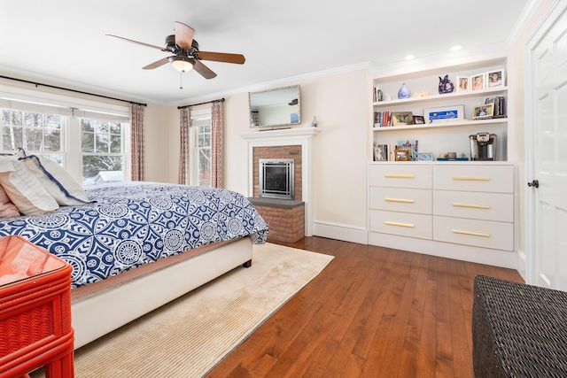 bedroom with a brick fireplace, a ceiling fan, dark wood finished floors, and crown molding