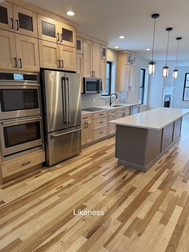 kitchen with stainless steel appliances, light countertops, glass insert cabinets, a sink, and a kitchen island