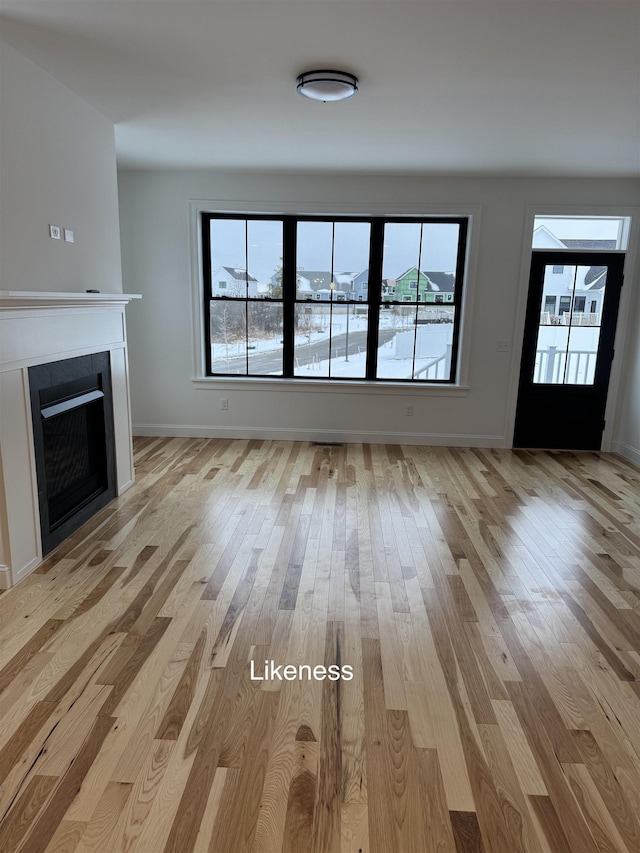 unfurnished living room featuring light wood-style floors, a fireplace with flush hearth, baseboards, and a wealth of natural light