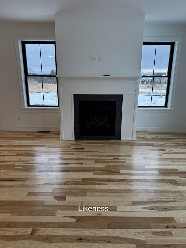 unfurnished living room with baseboards, a fireplace, and light wood finished floors