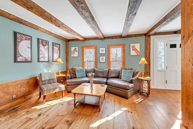 living room featuring visible vents, beamed ceiling, light wood-style flooring, and a healthy amount of sunlight