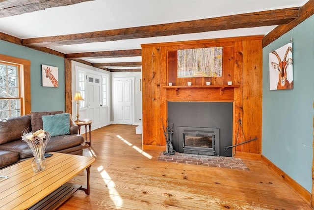 living area with beamed ceiling, a fireplace with flush hearth, light wood-style flooring, and baseboards